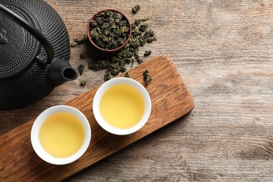 Cups and teapot of Tie Guan Yin oolong on wooden background, top view with space for text
