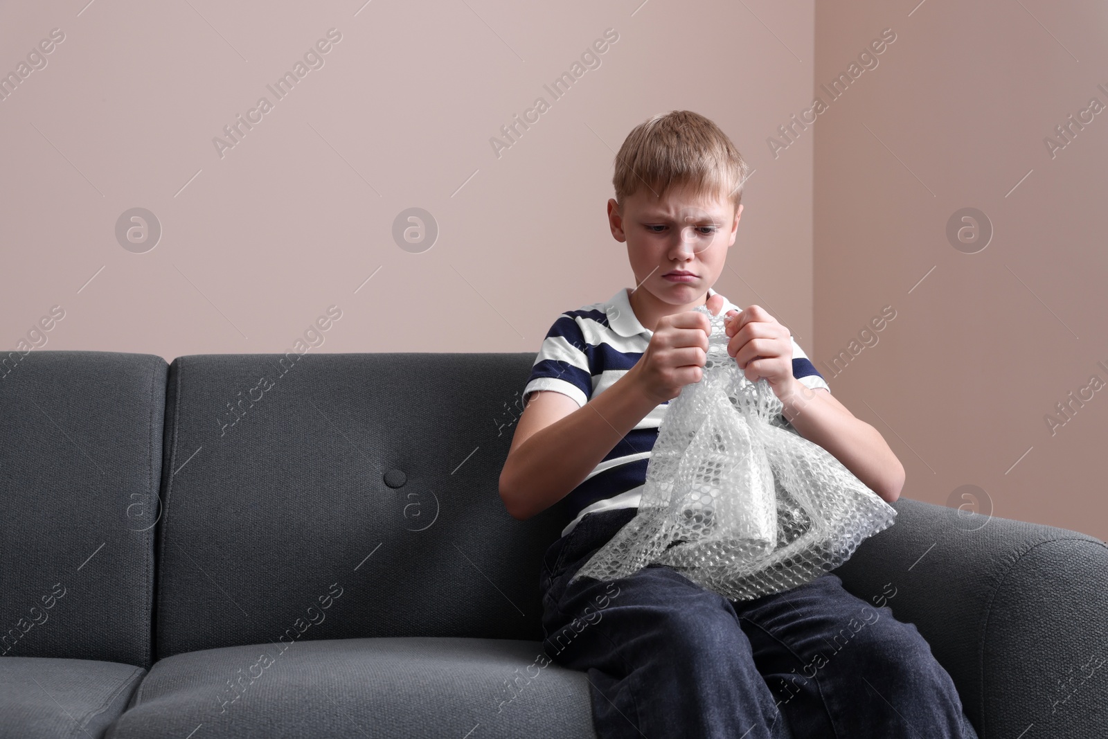 Photo of Emotional boy popping bubble wrap indoors. Stress relief