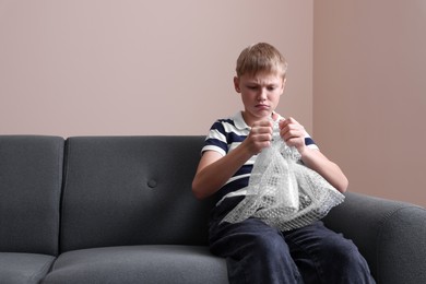 Photo of Emotional boy popping bubble wrap indoors. Stress relief