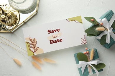 Photo of Beautiful wedding invitation card with Save the Date phrase, eucalyptus leaves, gift boxes and decor on white table, flat lay