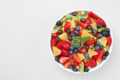 Photo of Yummy fruit salad in bowl on light background, top view. Space for text