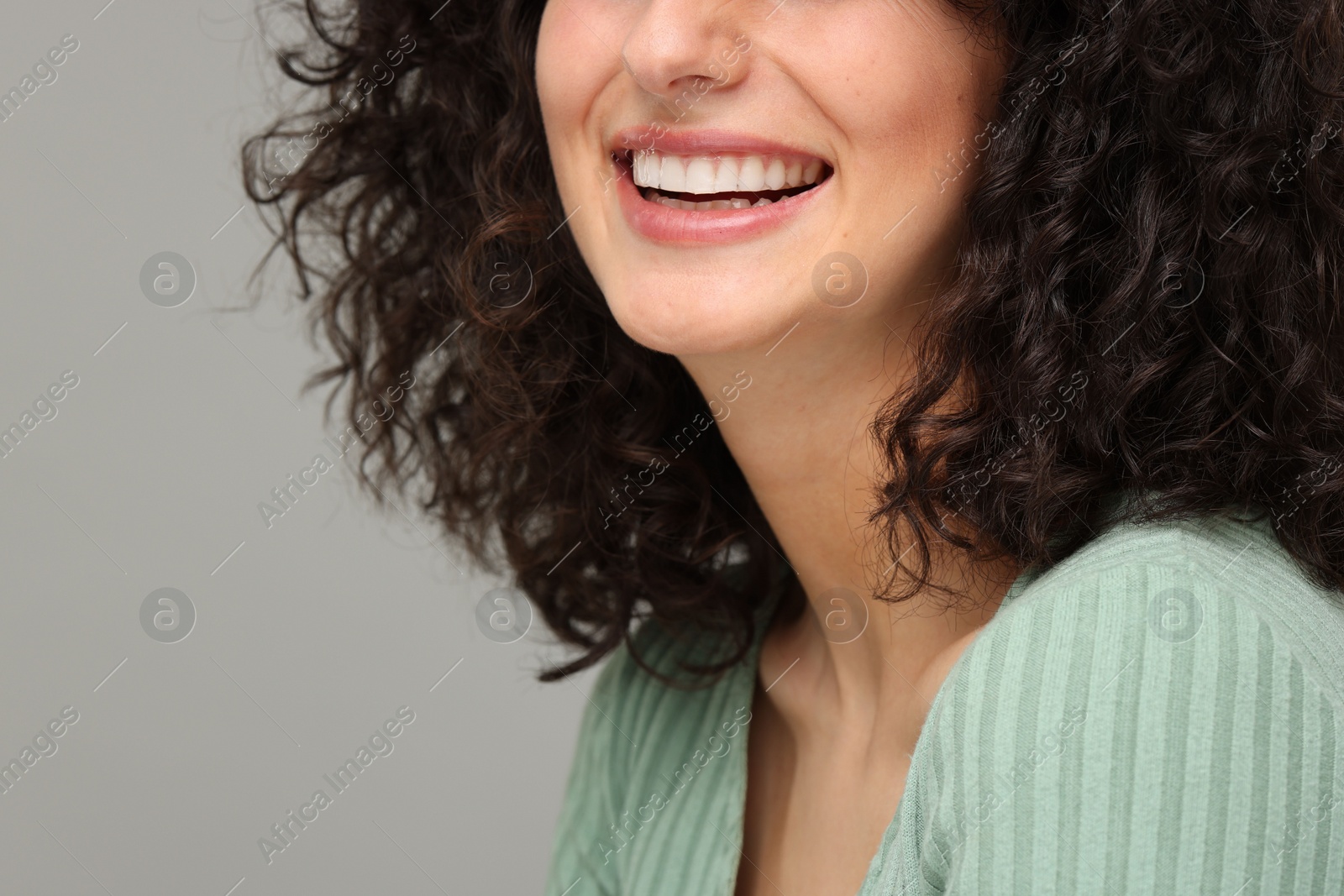 Photo of Young woman using teeth whitening strip on grey background, closeup. Space for text