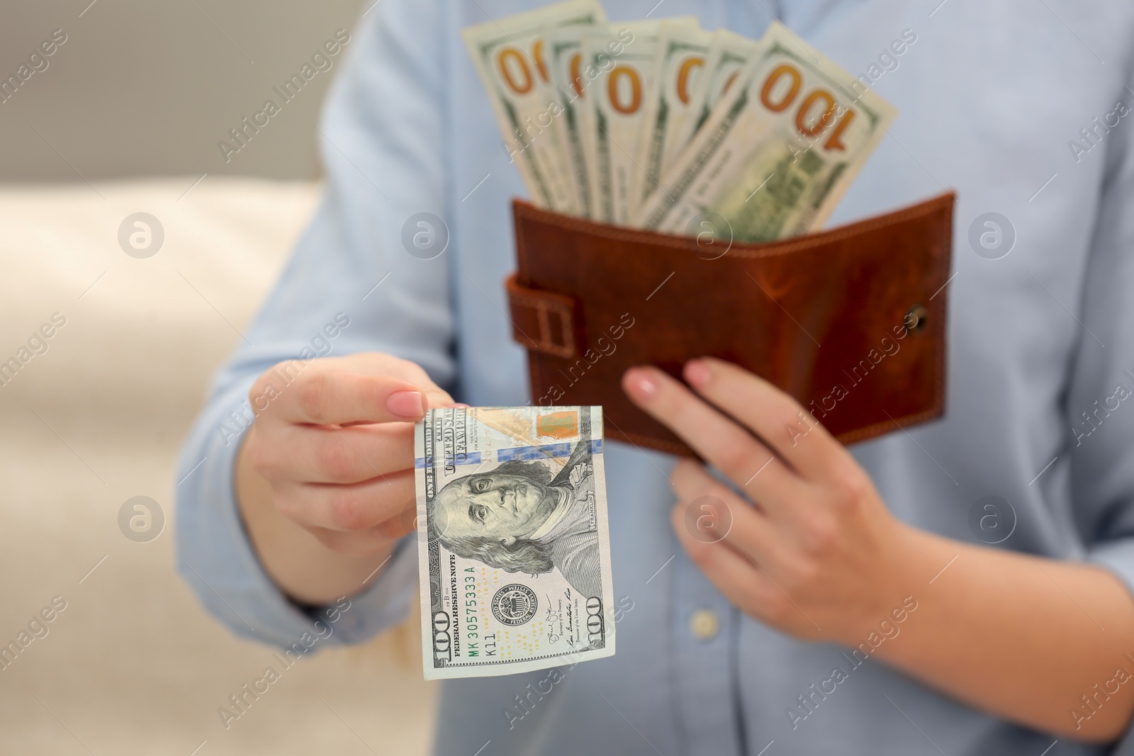 Photo of Woman giving 100 dollar bill and holding brown leather wallet with banknotes indoors, closeup. Money exchange