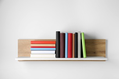 Many hardcover books on wooden shelf near white wall