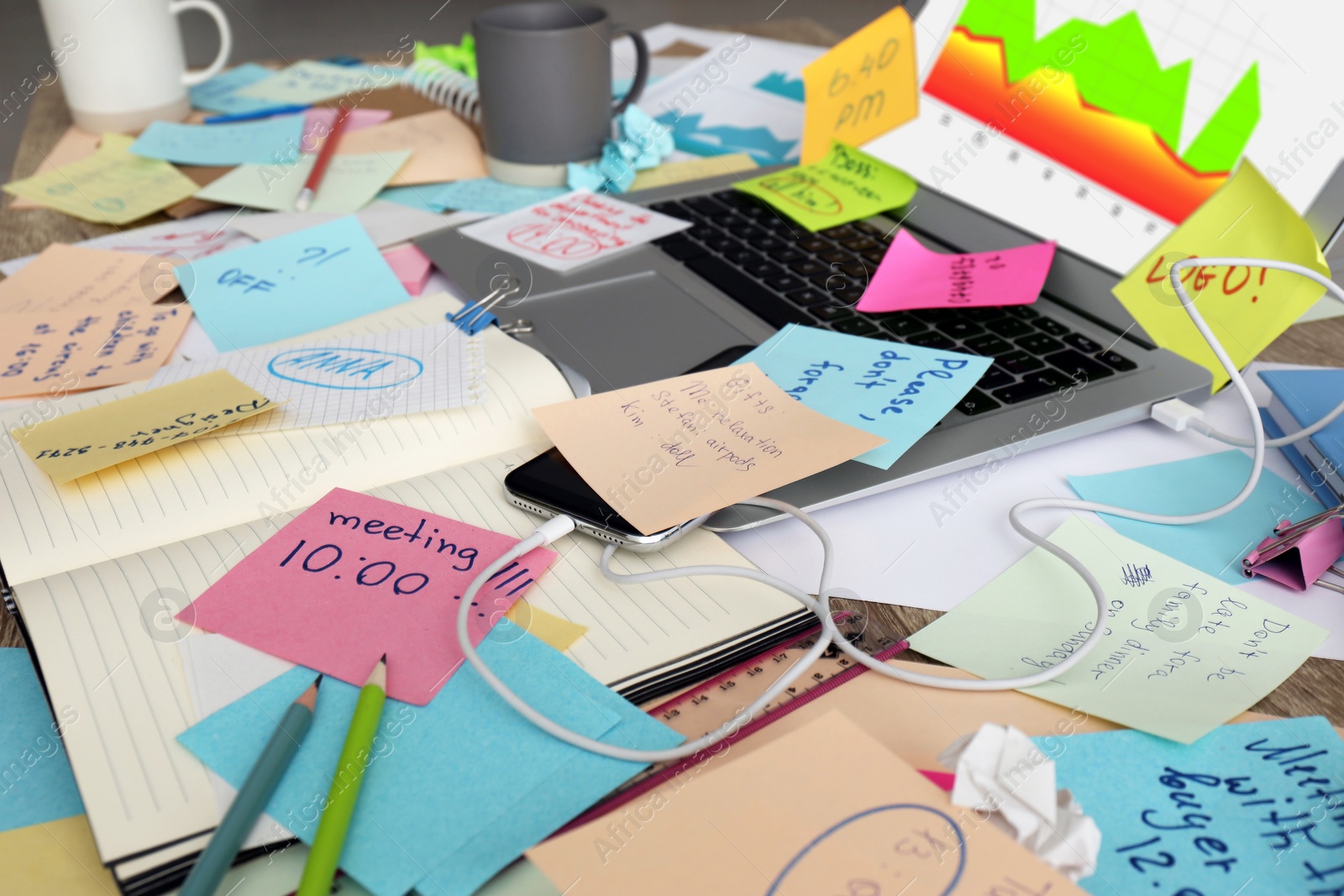 Photo of Laptop, notes and office stationery in mess on desk. Overwhelmed with work