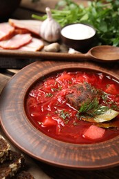 Photo of Stylish brown clay plate with Ukrainian borsch served on wooden table, closeup