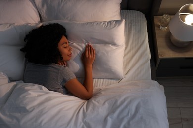 Young woman sleeping in soft bed at night, top view