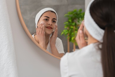 Photo of Young woman with headband washing her face near mirror in bathroom