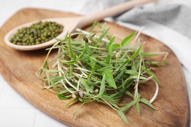 Photo of Wooden board with mung beans and sprouts on light table, closeup
