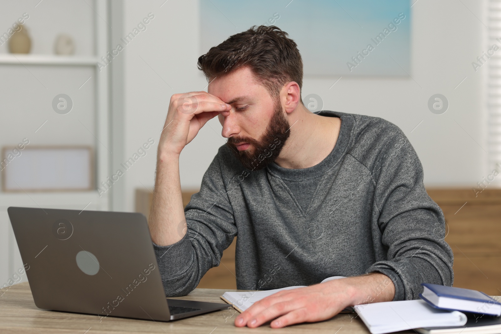 Photo of Overwhelmed man sitting with laptop at table indoors