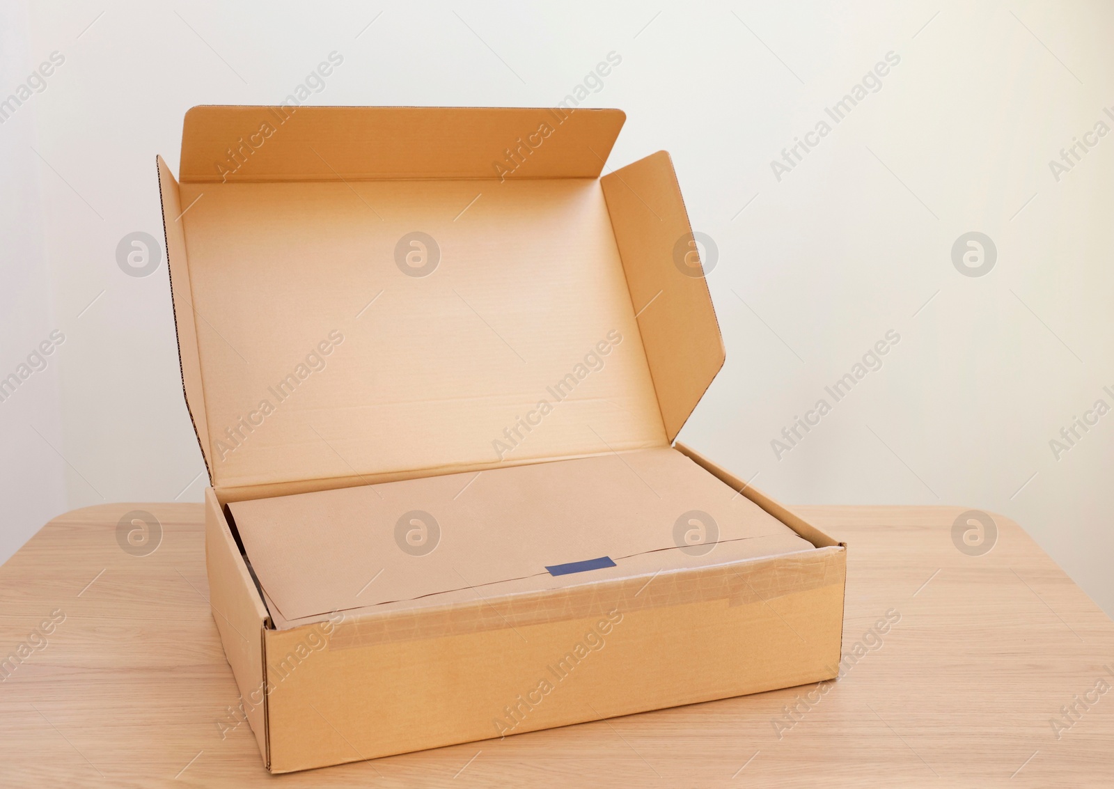 Photo of Open cardboard box with item wrapped in kraft paper on wooden table, space for text. Delivery service