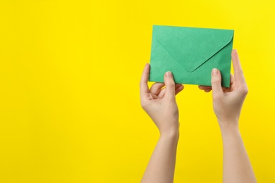 Woman holding green paper envelope on yellow background, closeup. Space for text