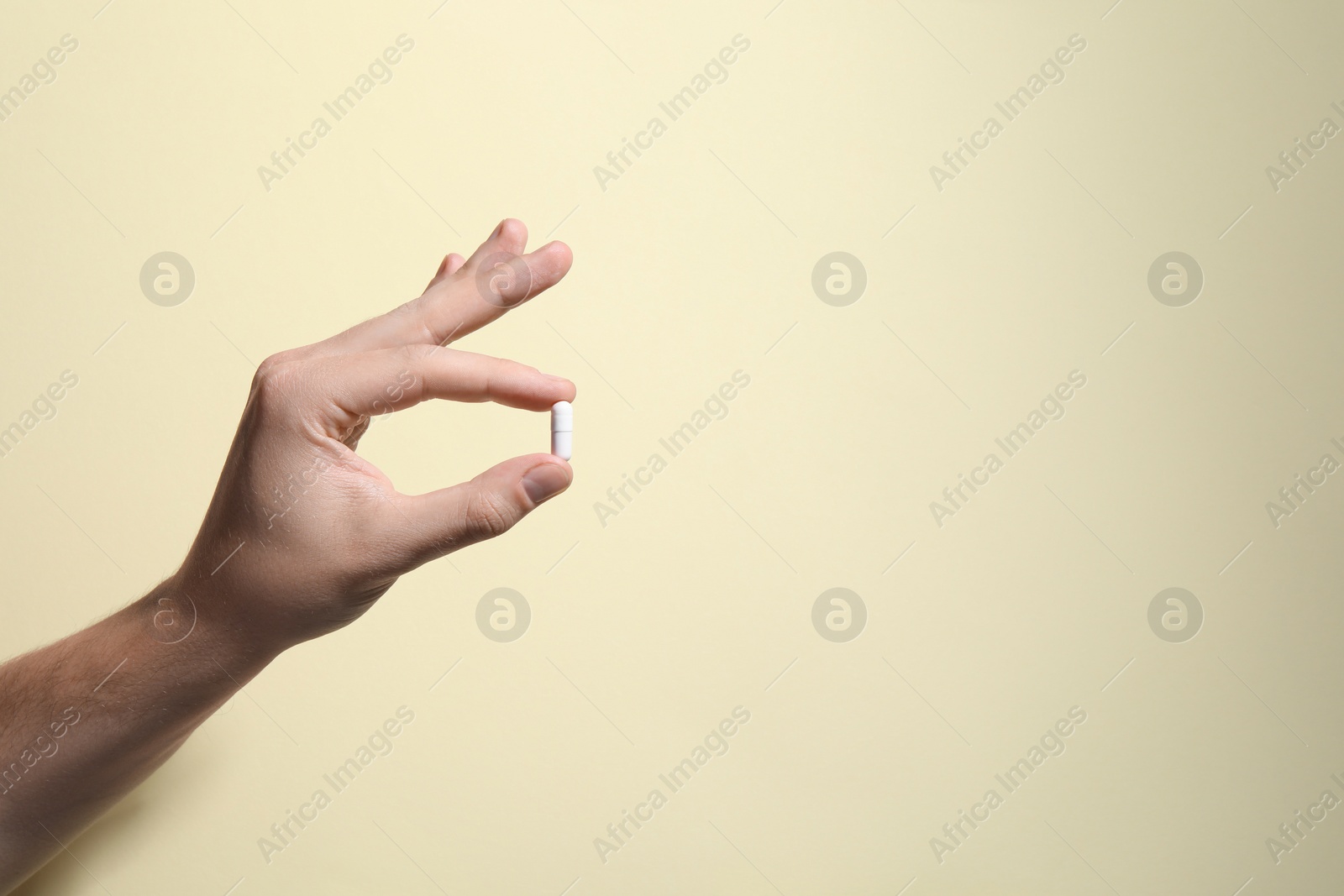 Photo of Man holding pill on beige background, closeup. Space for text