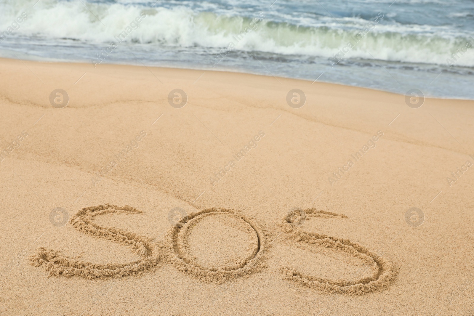 Photo of Message SOS drawn on sand near sea