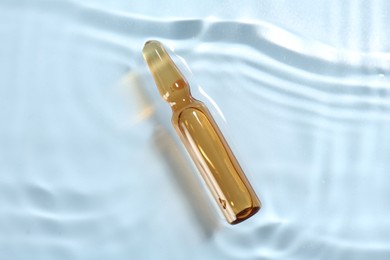 Skincare ampoule in water on light blue background, top view