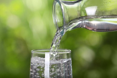 Photo of Pouring water from bottle into glass on blurred green background, closeup
