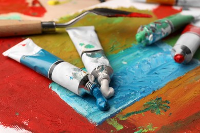Photo of Tubes of colorful oil paints and spatula on canvas with abstract painting, closeup