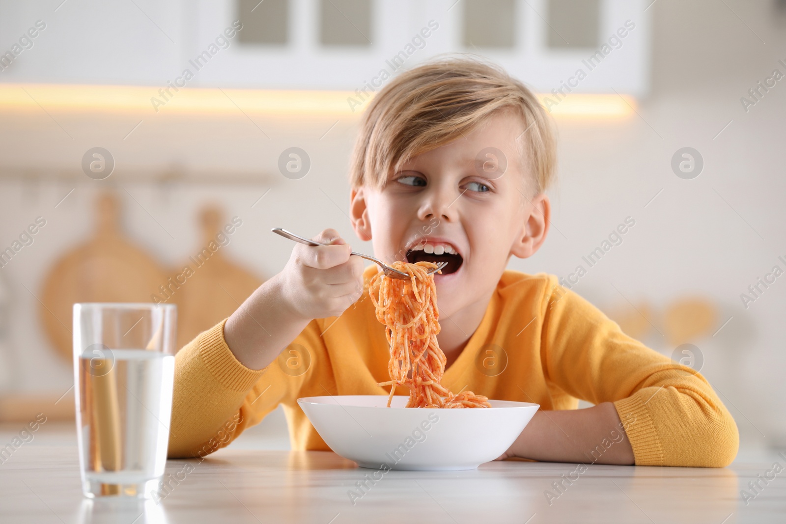 Photo of Happy boy eating tasty pasta at table in kitchen