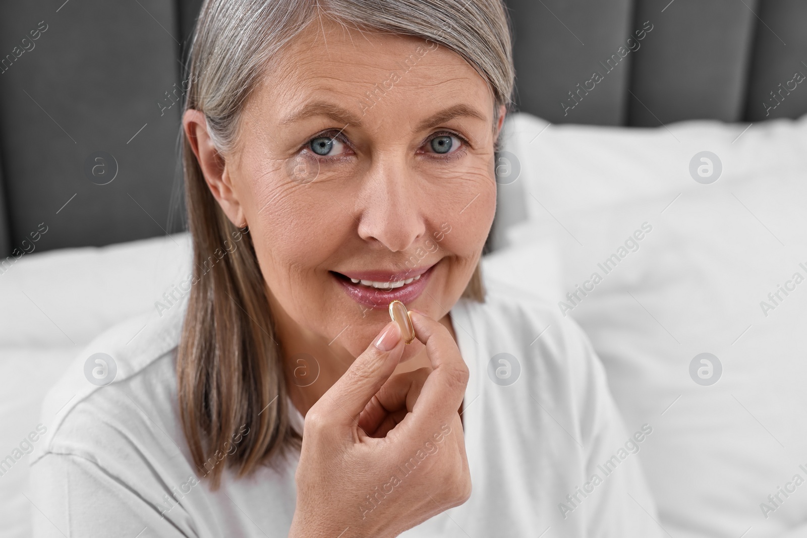 Photo of Beautiful woman taking vitamin pill in bedroom