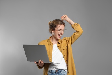 Portrait of emotional woman with modern laptop on grey background