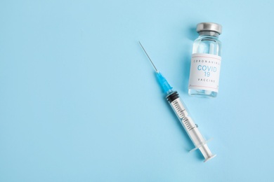 Photo of Vial with coronavirus vaccine and syringe on light blue background, flat lay. Space for text