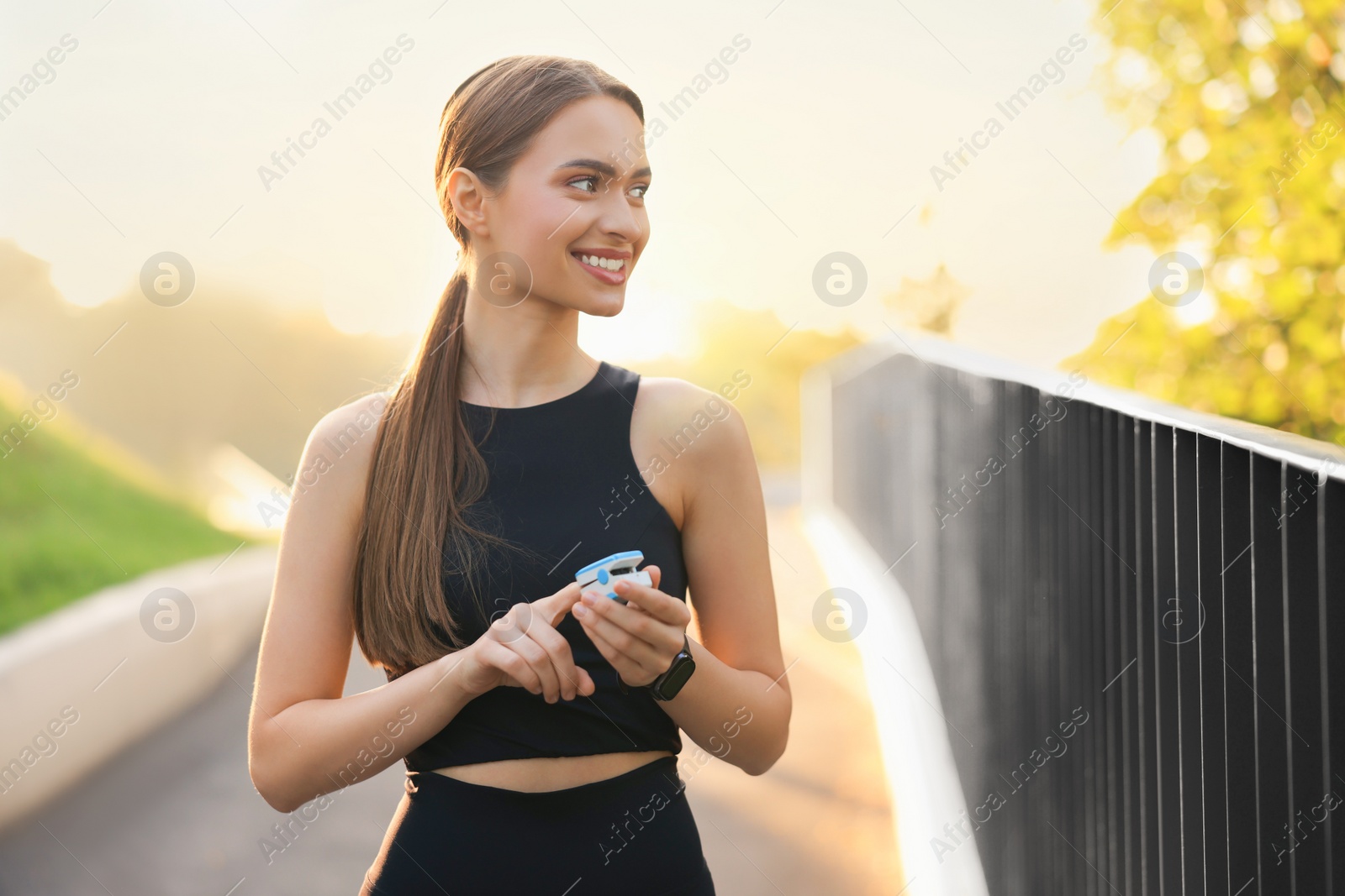 Photo of Happy woman checking pulse with blood pressure monitor on finger after training outdoors. Space for text