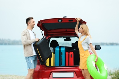 Couple packing suitcases in car trunk on riverside