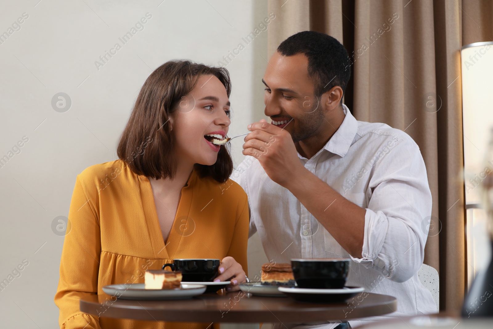 Photo of Romantic date. Guy feeding his girlfriend with cheesecake in cafe