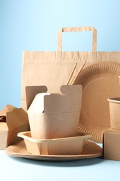 Photo of Eco friendly food packaging. Paper containers, tableware and bag on white table against light blue background