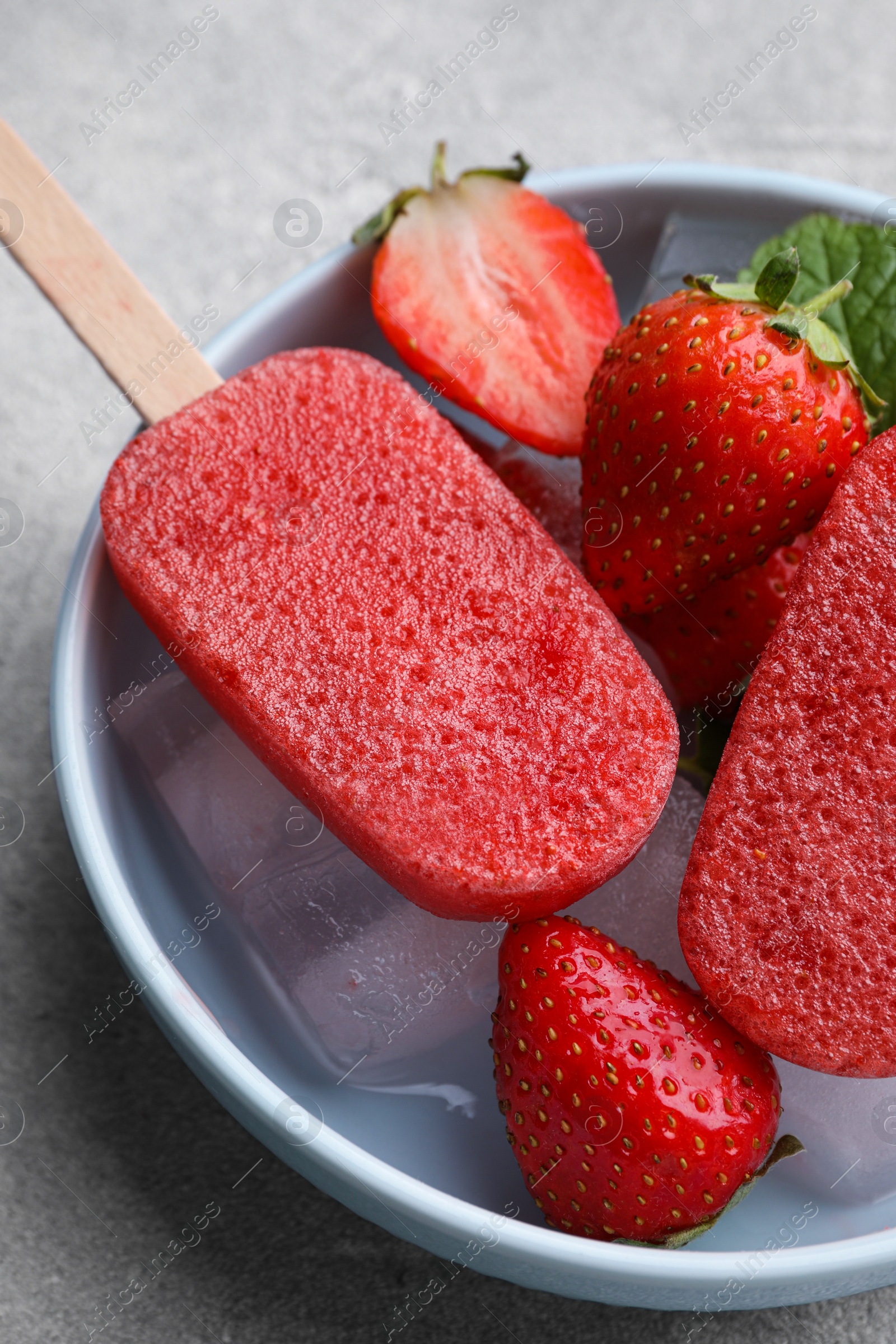 Photo of Bowl of tasty strawberry ice pops on grey table, closeup. Fruit popsicle
