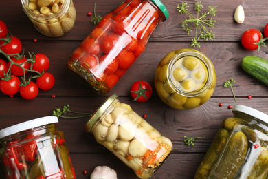 Jars of pickled vegetables and ingredients on wooden table, flat lay