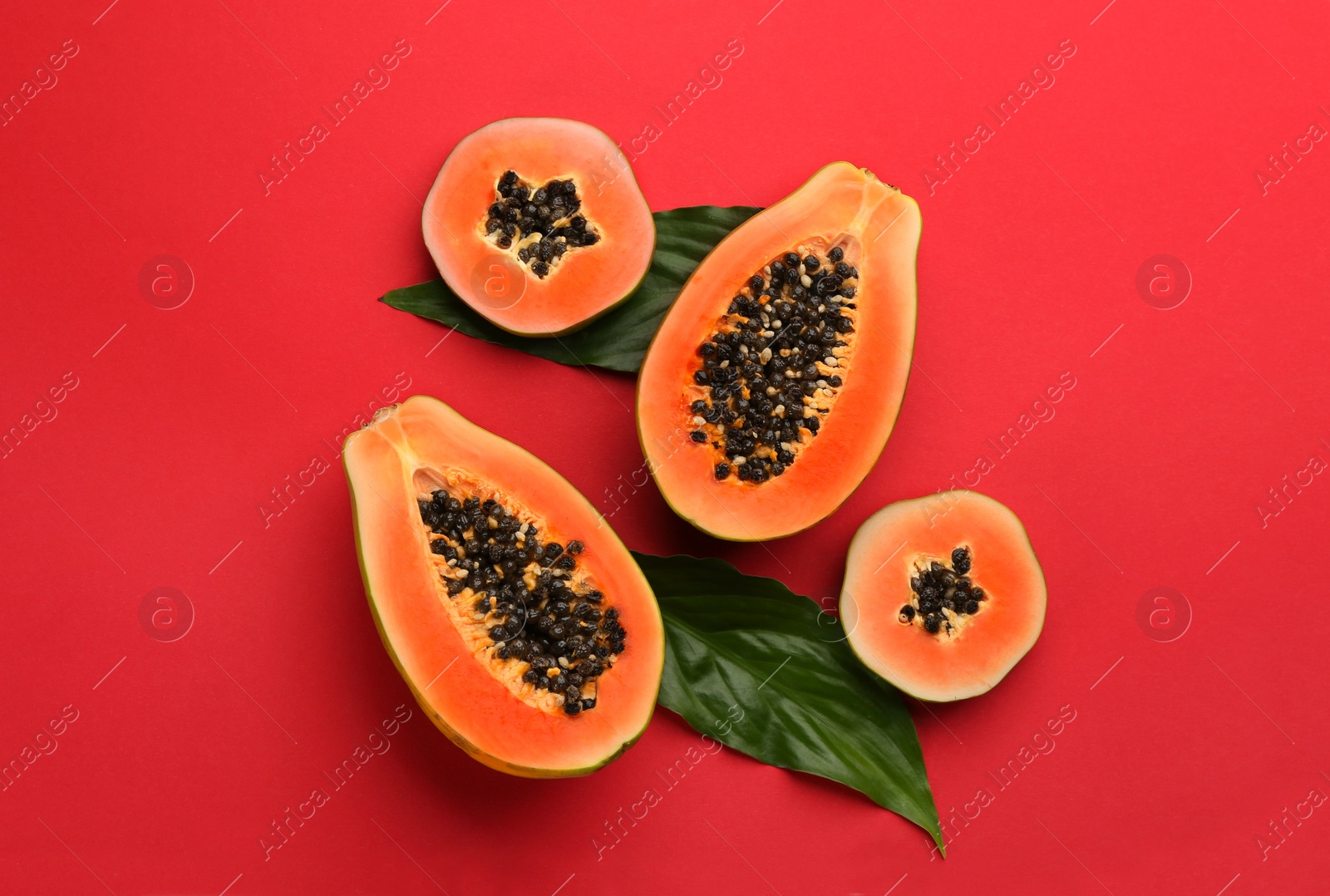 Photo of Fresh ripe papaya fruits with green leaves on red background, flat lay
