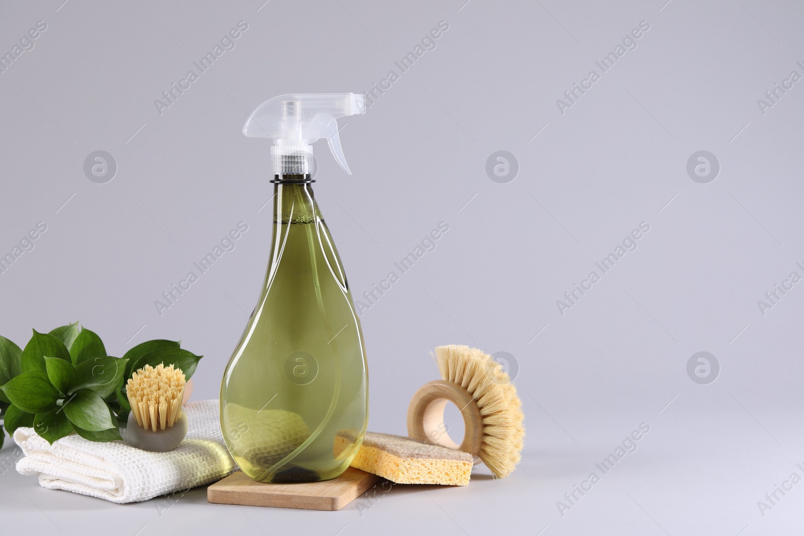 Photo of Bottle of cleaning product, rag, sponges and brushes on light grey background. Space for text