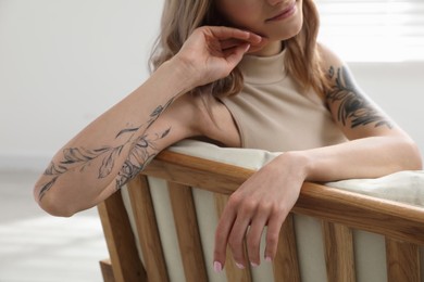 Photo of Beautiful woman with tattoos on arms resting indoors, closeup