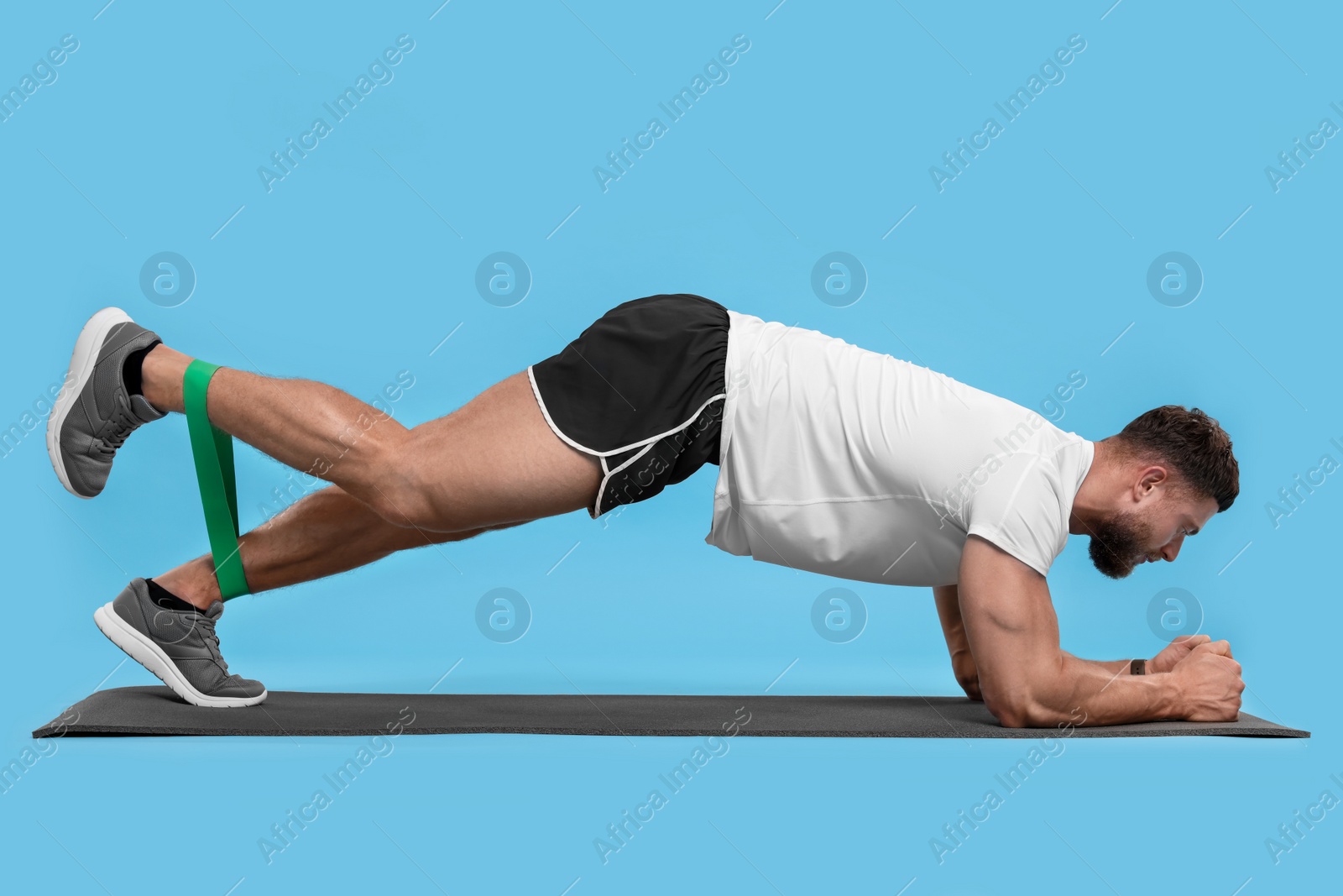 Photo of Young man exercising with elastic resistance band on light blue background