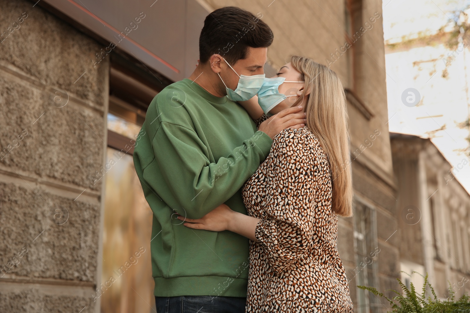 Photo of Couple in medical masks trying to kiss outdoors