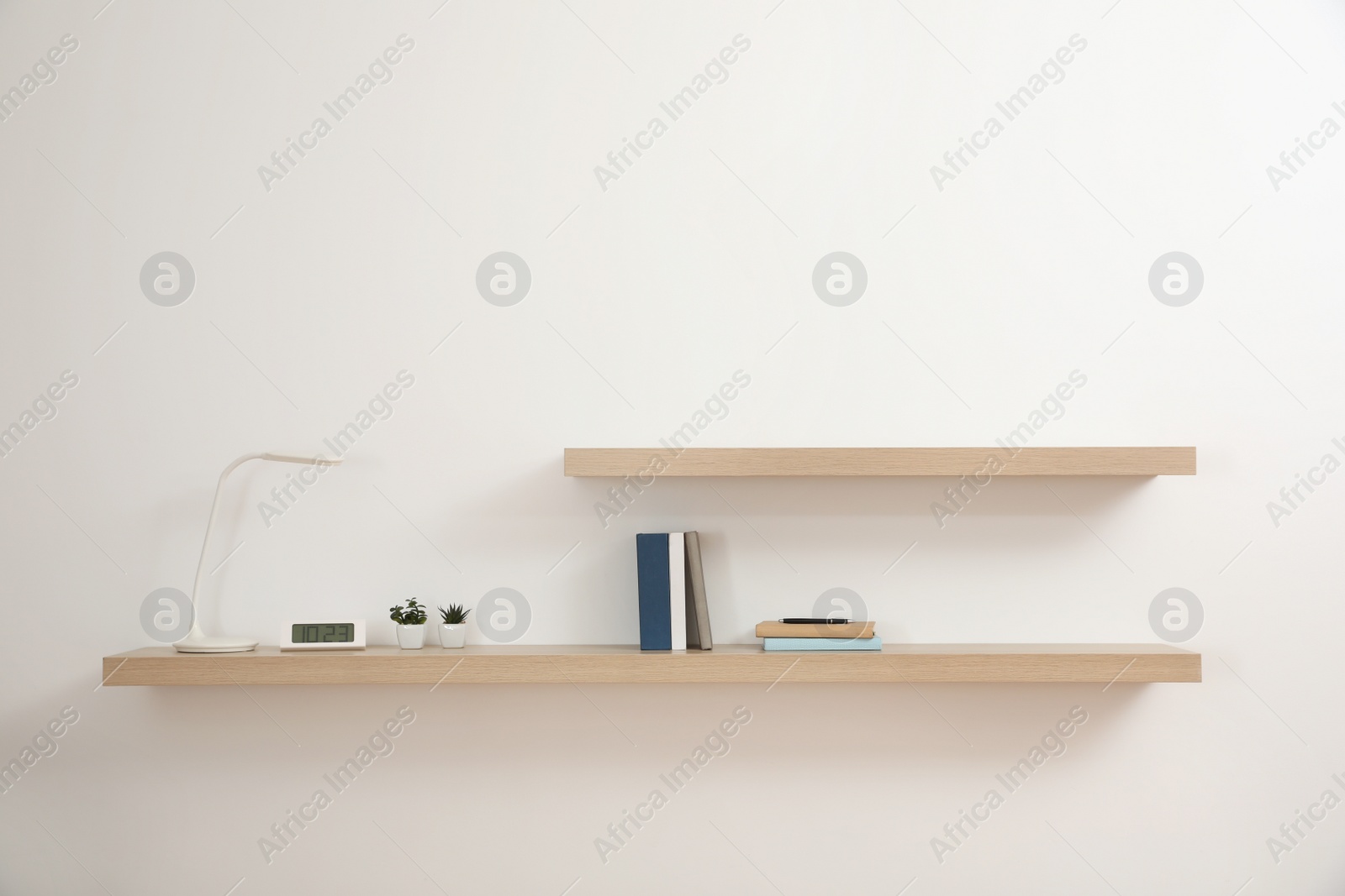 Photo of Wooden shelves with books and decorative elements on light wall