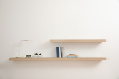 Photo of Wooden shelves with books and decorative elements on light wall