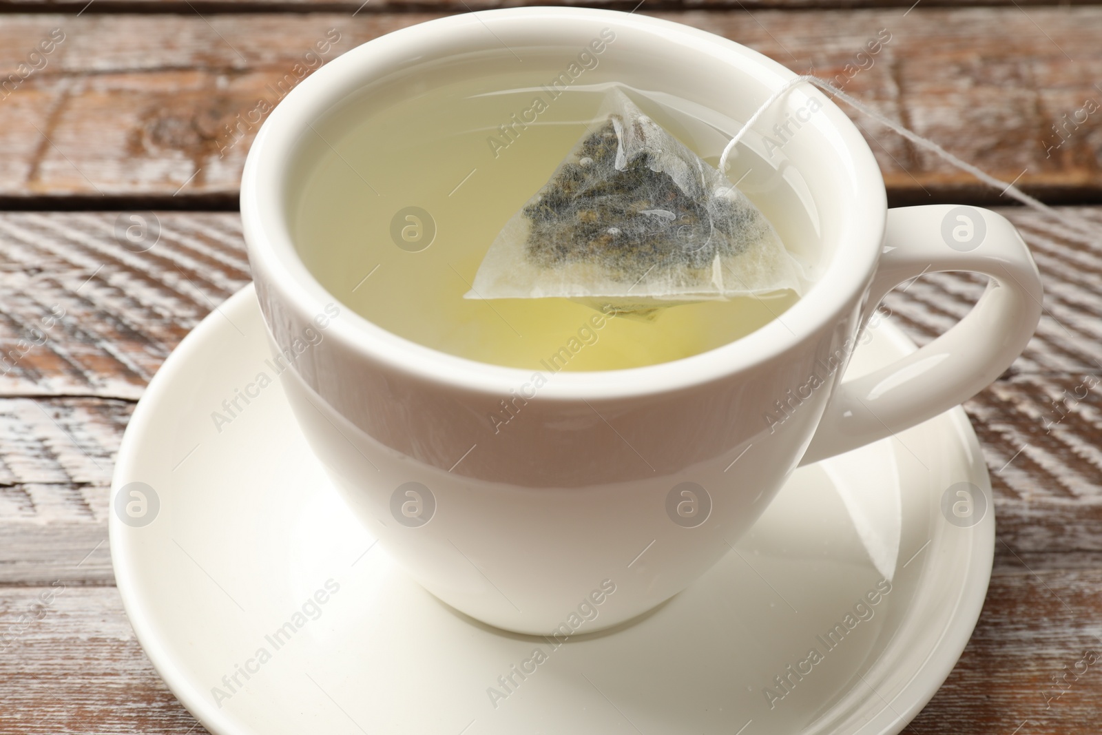 Photo of Tea bag in cup with hot drink on wooden rustic table, closeup