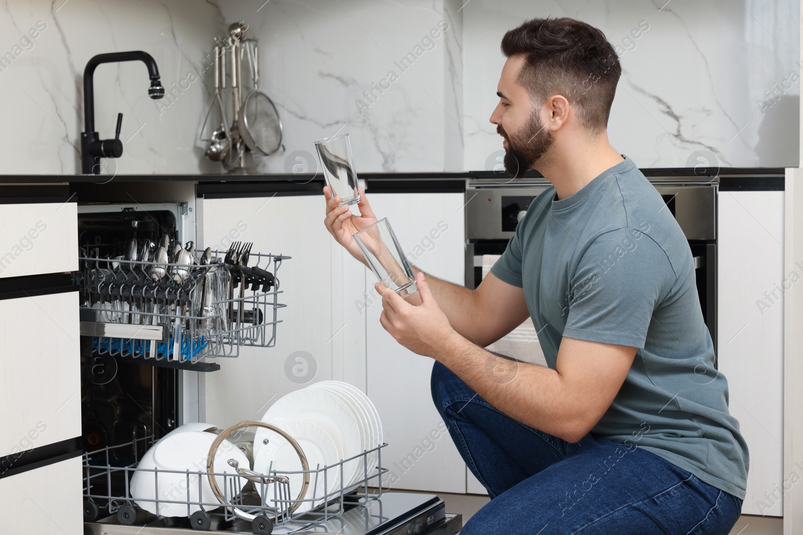 Photo of Man loading dishwasher with glasses in kitchen