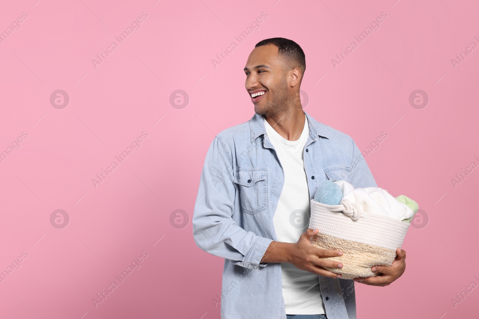 Photo of Happy man with basket full of laundry on pink background. Space for text