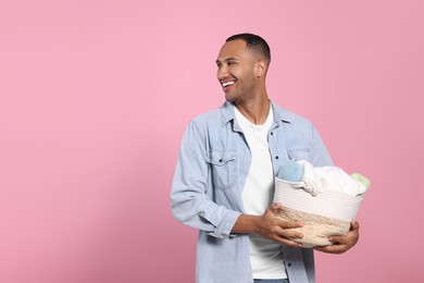 Photo of Happy man with basket full of laundry on pink background. Space for text