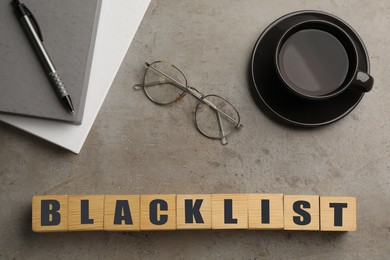 Photo of Wooden cubes with word Blacklist, cup of coffee and office stationery on grey table, flat lay