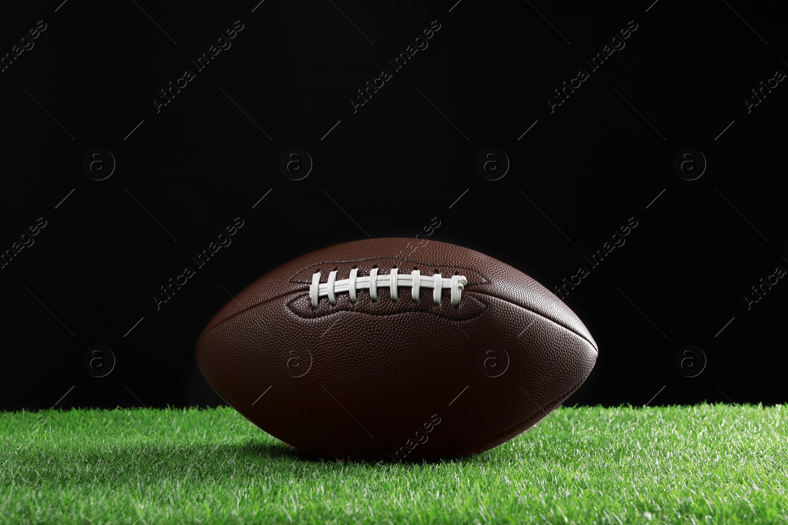 Photo of Leather American football ball on green grass against black background