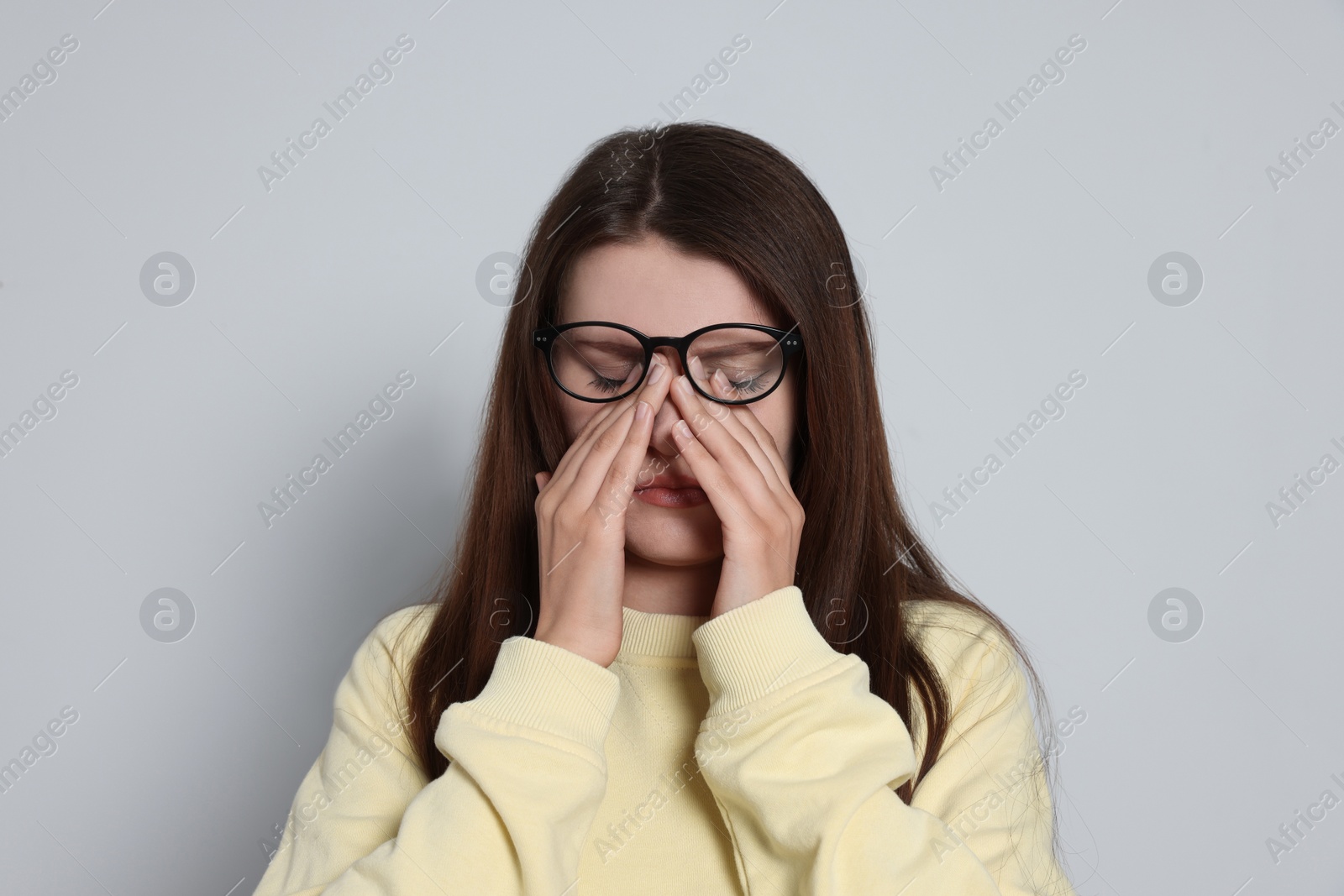 Photo of Young woman suffering from eyestrain on light background