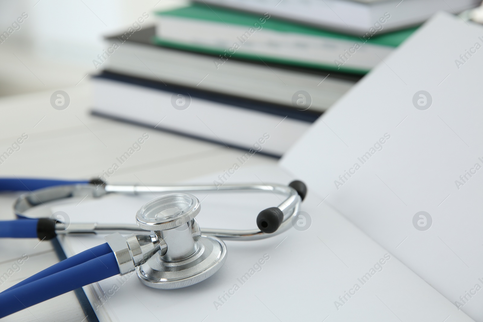 Photo of One new medical stethoscope and books on white table, closeup