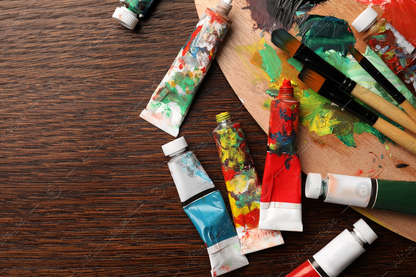 Photo of Tubes with oil paints, brushes and palette on wooden table, flat lay. Space for text