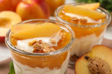 Photo of Tasty peach yogurt with granola, pieces of fruit and jam on table, closeup