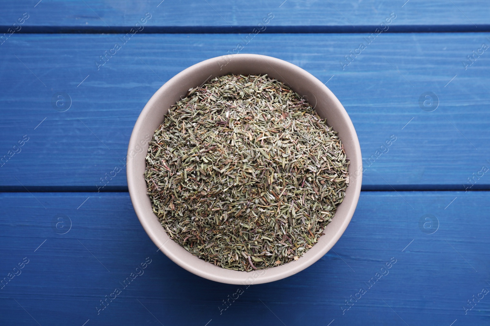 Photo of Bowl with dried thyme on blue wooden table, top view