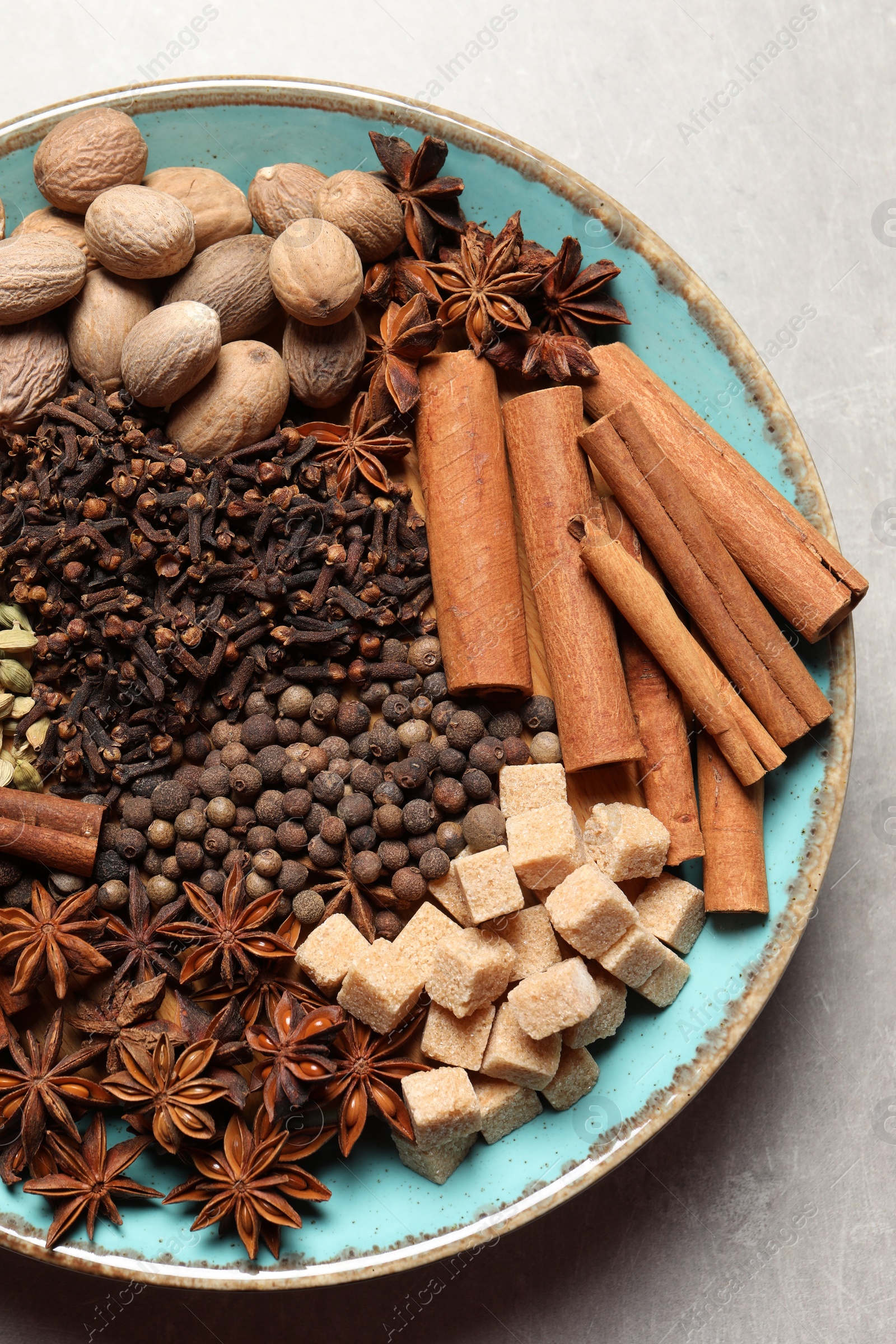 Photo of Different spices and nuts in bowl on light gray textured table, top view